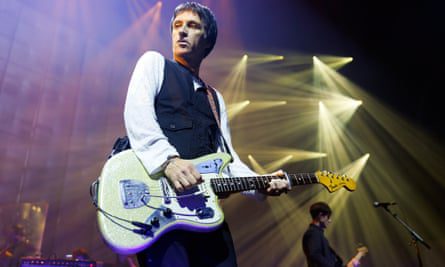 Johnny Marr plays guitar with stage lights behind him