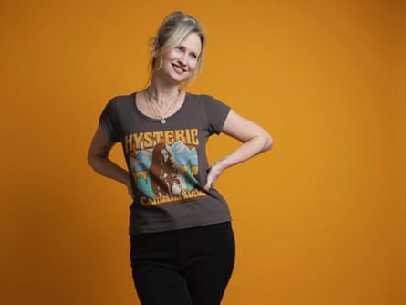 Lucy Nichol in a fun T-shirt, posing with her hands of her hips against an orange background