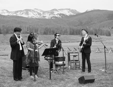 Black and white shot of Lekman with other band members playing instruments in a field in front of snow-capped mountains