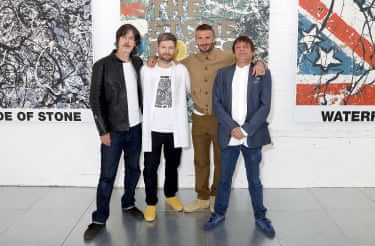 The men stand in front of Stone Roses artwork printed on the wall.