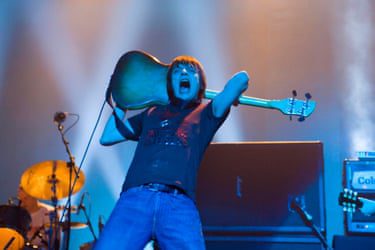 Mani roars as he holds his bass guitar over the back of his head.
