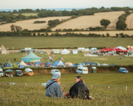 Fields with tents in the distance and a young couple sitting on the grass in the foreground.